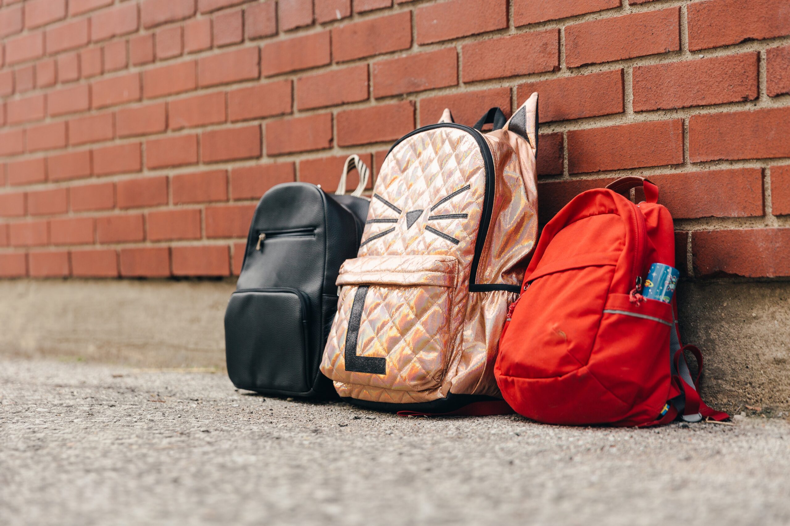 Three childrens backpacks and a brick wall